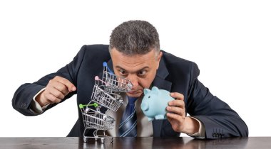 Takım elbiseli orta yaşlı bir adam, domuzcuk bnk ve boş minyatür market arabalarından oluşan bir piramit.