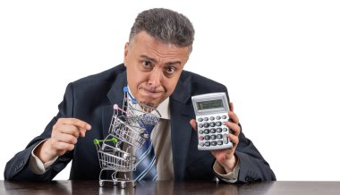 Takım elbiseli orta yaşlı bir adam, hesap makinesi ve boş minyatür market arabaları piramidi.