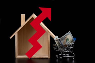 Minyatür ahşap ev, finansal haritadan kırmızı ok ve 100 dolar alışveriş arabası.