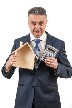 İş elbisesi, hesap makinesi ve sembolik ahşap ev giyen orta yaşlı bir adam.