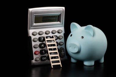 Mavi domuz kumbarası ve siyah arka planda merdiveni olan hesap makinesi