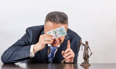 Takım elbiseli orta yaşlı bir adam, bir Themis figürü ve 100 Çek banknotu.