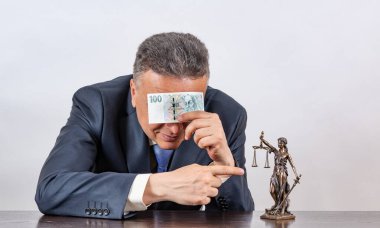 Takım elbiseli orta yaşlı bir adam, bir Themis figürü ve 100 Çek banknotu.