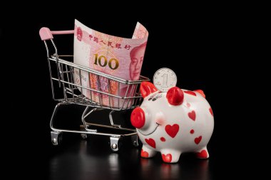 1 Çin Yuan sikkesi, domuz kumbarası ve 100 Yuan banknot ve siyah arka planda Başkan Mao portresi.