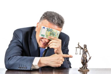 Takım elbiseli orta yaşlı bir adam gözlerini 100 Euro 'luk banknotun ve Themis' in bir figürünün arkasına saklar.