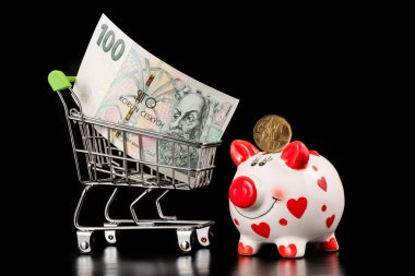 Minyatür süpermarket alışveriş arabasında 100 altın banknot domuz kumbarası ve siyah arka planda 20 Çek kuruşu.