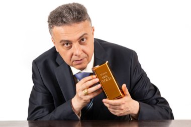 Takım elbiseli orta yaşlı bir adam elinde 999 altın külçesi tutuyor.