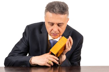 Takım elbiseli orta yaşlı bir adam elinde 999 altın külçesi tutuyor.