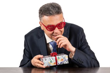 İnsan kalbi sembollü gözlük takan orta yaşlı bir işadamı. İçinde 100 dolarlık banknot resmi olan bir hediye kutusu var.