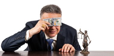 Takım elbiseli orta yaşlı bir adam gözlerini 100 dolarlık banknotun ve beyaz arka planda bir Themis figürünün arkasına saklar.