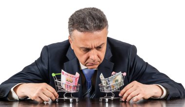 Orta yaşlı takım elbiseli bir adam ve 100 porselen yuan ve beyaz arka planda 100 dolarlık minyatür alışveriş arabaları.