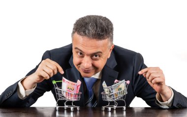 Orta yaşlı takım elbiseli bir adam ve 100 porselen yuan ve beyaz arka planda 100 dolarlık minyatür alışveriş arabaları.