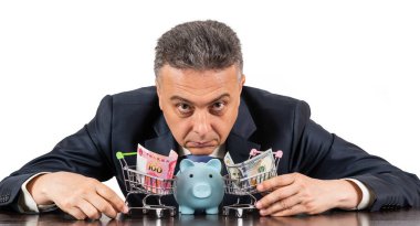 Orta yaşlı takım elbiseli bir adam ve 100 porselen yuan ve beyaz arka planda 100 dolarlık minyatür alışveriş arabaları.