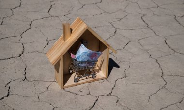 10,000 Kazakistan tenge minyatür bir süpermarket alışveriş arabasında ve ahşap evde çöldeki sıcak, çatlak kil zeminine karşı.