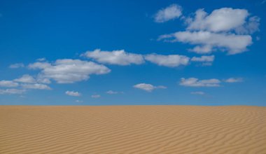 Kum tepeciğinin üstündeki mavi gökyüzünde bulutlar