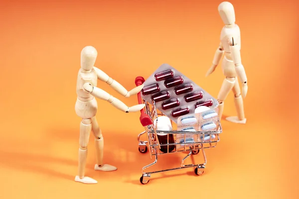 Dummy pushing a shopping trolley with medicines on an orange background. Health and medicine concept