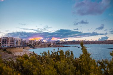 Malta adasındaki Saint Paul Koyu 'nda güzel bir akşam. Önplanda güzel binalar, gökyüzü ve çiçekler var..