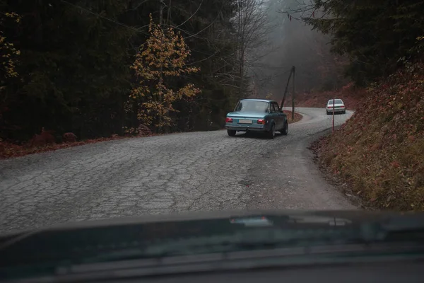 一排排老式汽车在弯弯曲曲的路上行驶 七十年代的赛车在森林里一排排跑着 — 图库照片