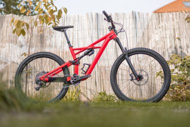 Side view of a modern mountain bike or bicycle for off road. Enuduro mtb bicycle parked on a lawn. Red MTB standing upright on grass, static, no people.