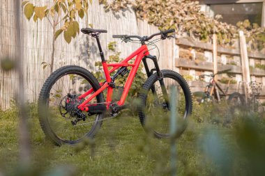 Side view of a modern mountain bike or bicycle for off road. Enuduro mtb bicycle parked on a lawn. Red MTB standing upright on grass, static, no people.