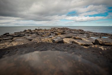 Kuzey İrlanda 'daki Giants geçidinde altıgen taş panorama ya da sütunlar bulutlu bir günde plajda görkemli bazalt sütunlar. Alanın geniş görünümü..