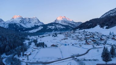 Güneşli bir kış gününde İtalyan Dolomitler 'in Sappada köyünün insansız hava aracı panoraması karla doludur. Dolomitlerin güzel dağlık köyü.