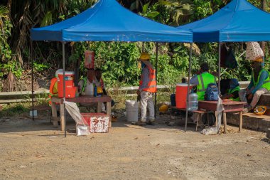 Siquirres, Kosta Rika, 28.4.2023: Yerel yol işçileri sıcak bir yaz gününde çadırların yaptığı bir gölgede dinleniyorlar. İnşaat alanındaki işçilerin korunması.