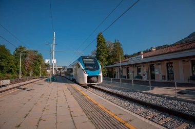 Günümüz EMU treni güneşli bir yaz gününde Rimske Toplice tren istasyonuna geliyor. Gölgesiz modern platform.