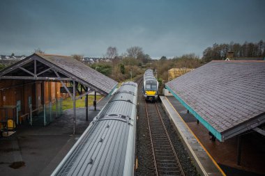 Kuzey İrlanda 'daki Ballymoney tren istasyonundan iki dizel tren geçiyor. Yaya geçidinden trenlere ve tren raylarına doğru bakıyorum..