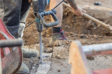 Erkekler, yenileme ya da tedavi sürecinin bir parçası olarak zemin ya da yolun parçalarını kaldırmak için balyoz ya da elektrikli keski kullanıyorlar..