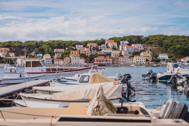 Güneşli bir sonbahar gününde, marinadaki Mali Losinj Koyu 'nun üzerinde yükselen evlerin manzarası. Ön planda farklı tekneler var..