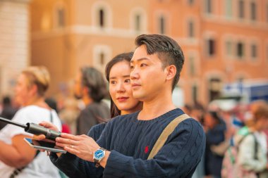 ROME, ITALY, 31.10.2023: Asyalı çift, Roma 'nın merkezindeki Sixtine Şapeli' nin çömelmiş anıtının önünde selfie çubuğu kullanarak selfie çekiyor..