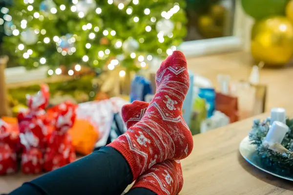 Lazy person wearing christmas style socks, resting and also being too lazy to open presents for christmas seen in the background.