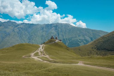 Kazbegi Üçlemesi, büyülü bir kilise ve Gürcistan dağlarında yüksek bir yerde ibadet yeri. Uzak, görkemli arkaplandan görüntüle.