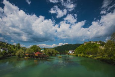 Bosanska Krupa 'daki Una nehri üzerindeki köprü, arka planda bazı rıhtımlara ve kalelere bakıyor. Bosna 'nın güzel manzarası, mavi gökyüzü.