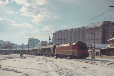 Modern kırmızı lokomotifli yük treni Ljubljana istasyonundan ayrılıyor ve soğuk bir kış gününde kuzeye doğru yola devam ediyor..