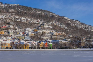Bergen 'de kışın tipik evler, Bergen sokaklarında soğuk kış günü, yollar karla kaplı ve göl kenarındaki uzun renkli evler.