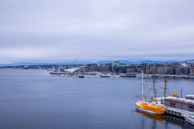 Askerhus Kalesi 'nden şehrin Aker Brygge bölgesine doğru lüks tekneler demirlemiş ve arkasında fantastik bir mimari ile manzara. Bulutlu kış günü.