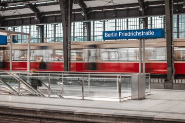 Berlin Friedrichstrasse adlı tren istasyonunun panolarını göster. Eski moda tren istasyonu, çift katlı yolcu treni hareket bulanıklığında hareket ediyor..