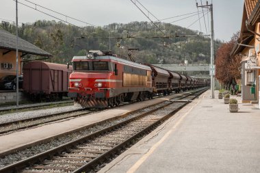 Krsko 'nun eski istasyonundan geçen bir yük treni. Kırmızı lokomotif, Dobova istikametindeki yük vagonlarını çekiyor. Güneşli nisan günü.