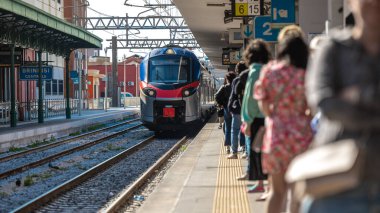 İnsanlar İtalya 'nın güneyindeki Brindisi, Puglia istasyonunda bir banliyö treninde, modern yolcu treninde bekliyorlar. Yoğun bir tren istasyonunda güneşli bir gün.