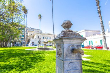 Brindisi 'deki virgilio parkındaki eski musluk, binalar ve arabalarla çevrili. Brindisi 'nin merkezine park et.