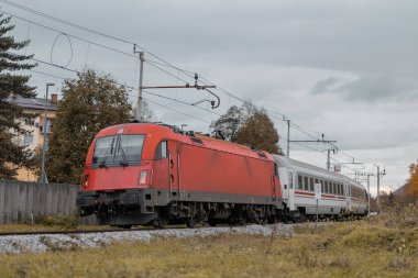 Arkada yolcu vagonları olan modern elektrikli çoklu voltaj lokomotifi. Uluslararası yolcu treni sonbaharda virajda