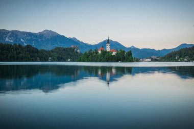 Slovenya 'daki Bled Gölü' nün huzurlu ve sakin fotoğrafı. Arka planda kale görünen bir gölün üzerindeki kilise manzarası..