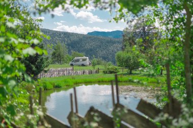 Güzel bir gölün önünde ve güzel bir dağ zemininin önünde park edilmiş küçük bir karavan ya da karavan. Doğada karavan destansı manzarası