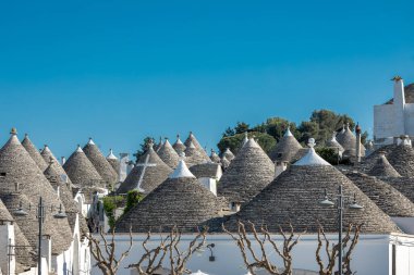 Güzel Alberobello şehrinin güney İtalya 'daki tipik taş çatıları. Taştan çatılar, biri beyaz haçla gösterilen bir kilise..