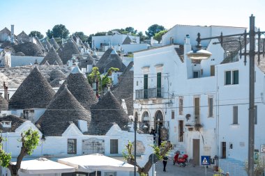 Güzel Alberobello şehrinin güney İtalya 'daki tipik taş çatıları. Taştan çatılar, biri beyaz haçla gösterilen bir kilise..