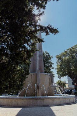 Vertical photo of Montuzza fountain in trieste hiding behind a row trees and sun star streak. Fountain on top of giants staircase above the carlo goldoni square clipart