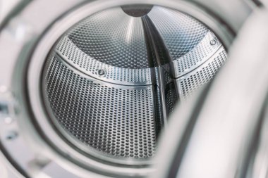 Endüstriyel bir çamaşır makinesinin içi. Görünür tırtıklı ya da delikli metal, parlak metal arka plan ve giysileri devirmek için çıkıntılar. Kapıyı aç.