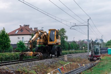 Lastik tekerlekleri ve tren tekerlekleri olan iki yönlü bir araç ya da kazıcı yenilenmek üzere olan bir demiryolunda dinleniyor..
